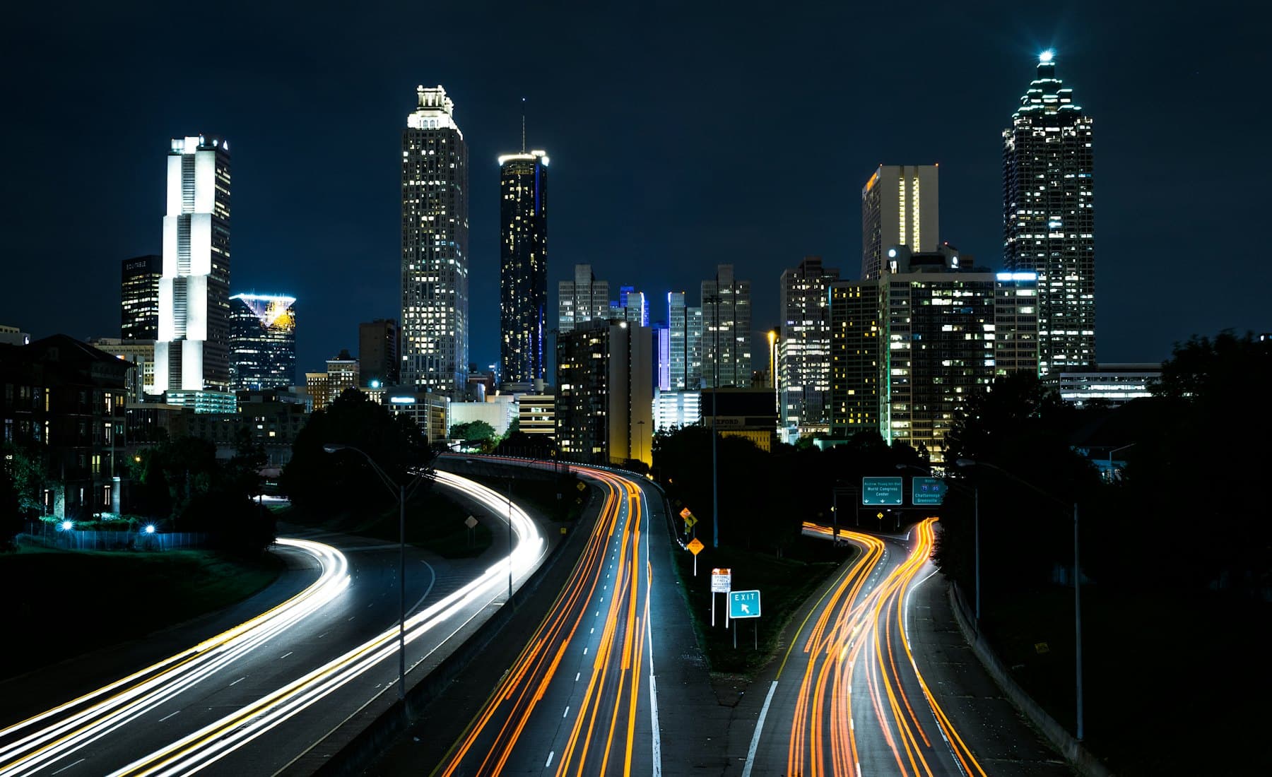 Interstate traffic streaking past a city skyline at night